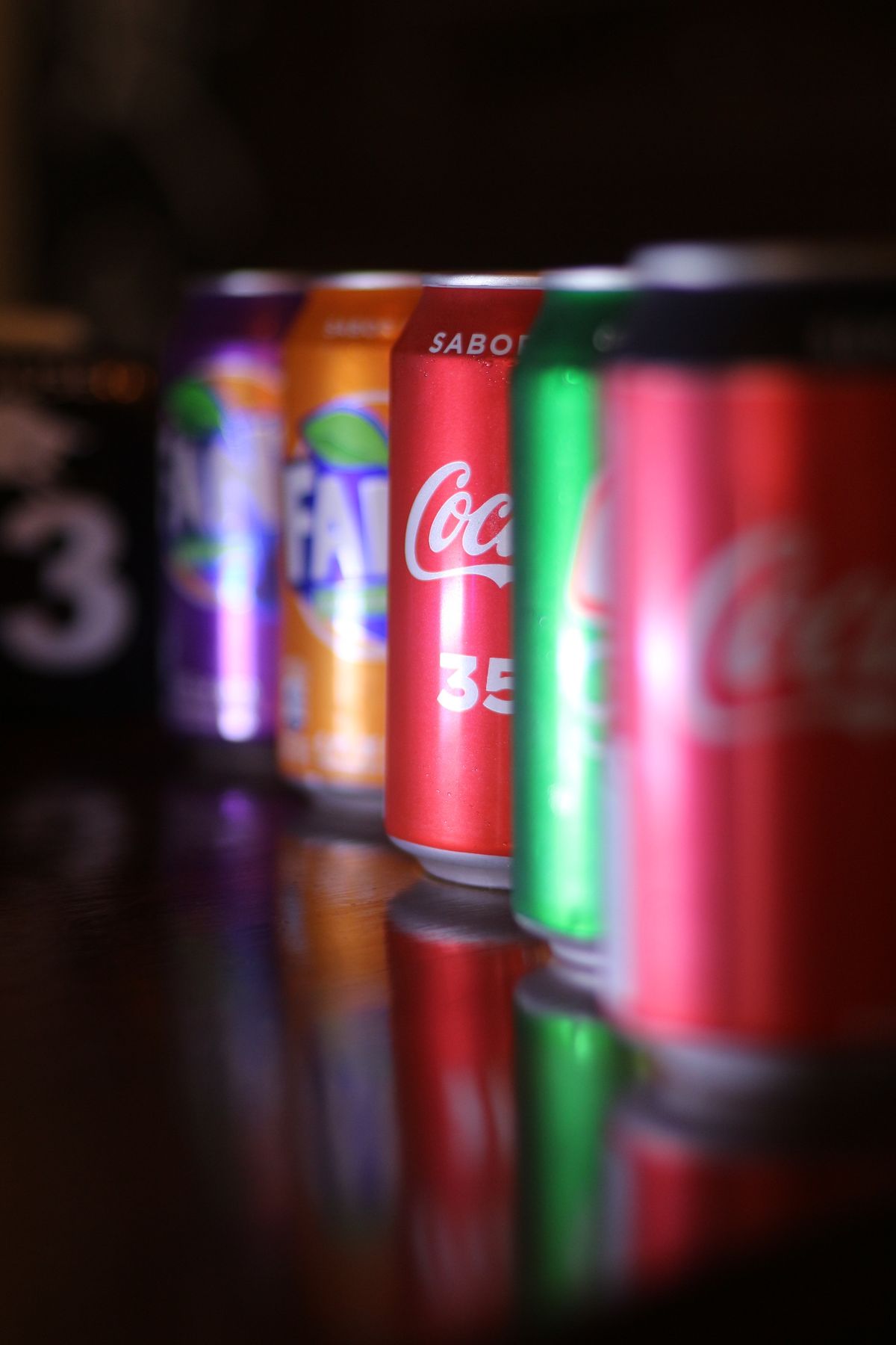Cans of energy drink and soda next to a close-up model of a tooth showing worn enamel
