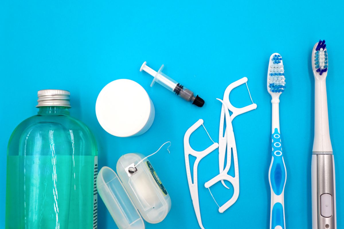 Bottle of mouthwash and a small measuring cup on a bathroom counter next to a toothbrush